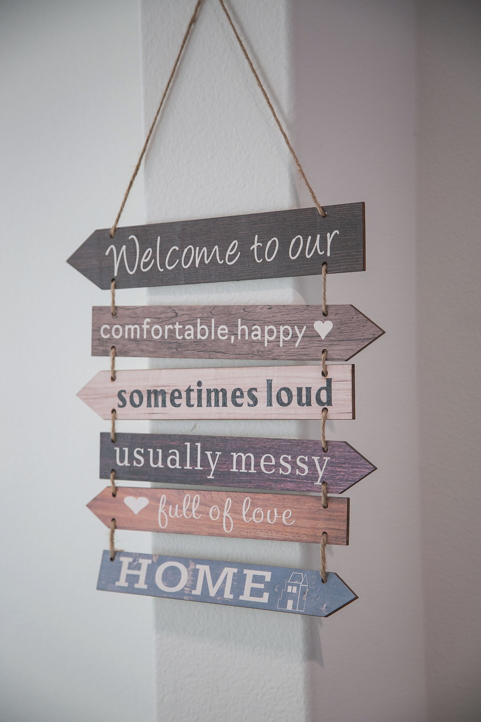 A wooden sign with phrases like "Welcome to our comfortable, happy sometimes loud usually messy full of love HOME" hanging on a wall.