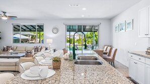 A spacious kitchen with granite countertops, a dining area with a table set for four, and a view of a pool through large windows.