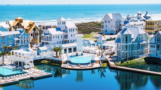 A coastal resort with multiple buildings, a central pool area, and a view of the ocean.
