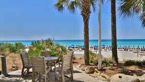 Un área de estar al aire libre con una mesa y sillas, con vistas a una playa con sombrillas y sillas de descanso.