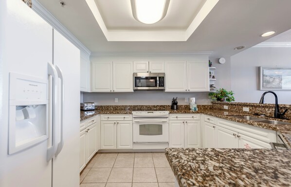 Una cocina moderna con armarios blancos, microondas integrado, estufa y encimeras de granito.