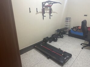 A small room with a treadmill, a bench, and a wall-mounted exercise equipment.