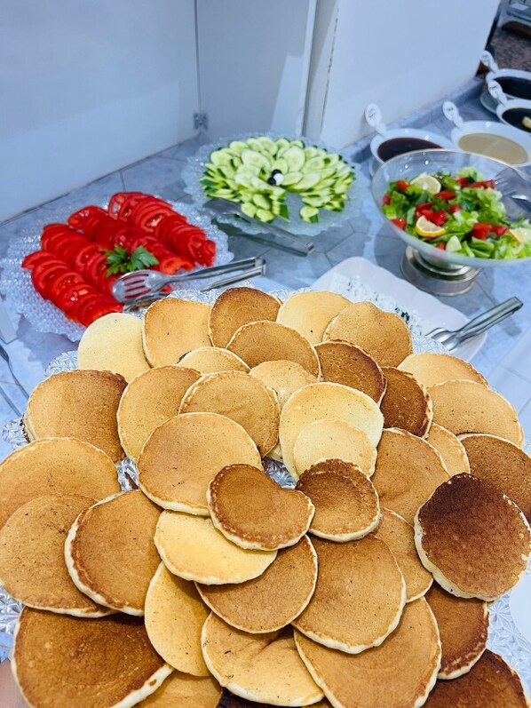 A table with a variety of food items including pancakes, a tomato salad, and a green salad. - ŞİRİN APARTROOMS (Denizli)