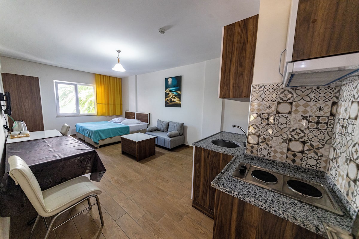 A compact room with a kitchenette, a dining area, and a bed.