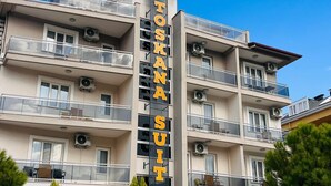 A multi-story hotel named "Toskan Suiten" with balconies, air conditioning units, and a clear blue sky. - ŞİRİN APARTROOMS (Denizli)