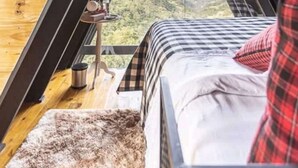 Een kamer in driehoekige vorm met een bed, een klein tafeltje en uitzicht op een bergachtig landschap.