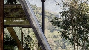 Een modern gebouw met een driehoekige kap, een glazen gevel, een open haard en uitzicht op een bergachtig landschap.
