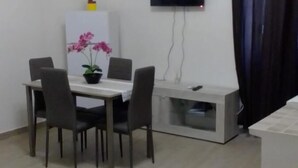 Pieni, siisti huone, jossa on ruokapöytä, tuoleja, televisio ja ruukussa oleva kasvi.