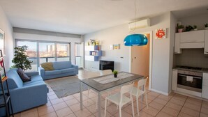 A modern living room with a sofa, a dining table, and a kitchen area. - Casa Adelaide, near the sea and the historic center with a panoramic terrace (Senigallia)
