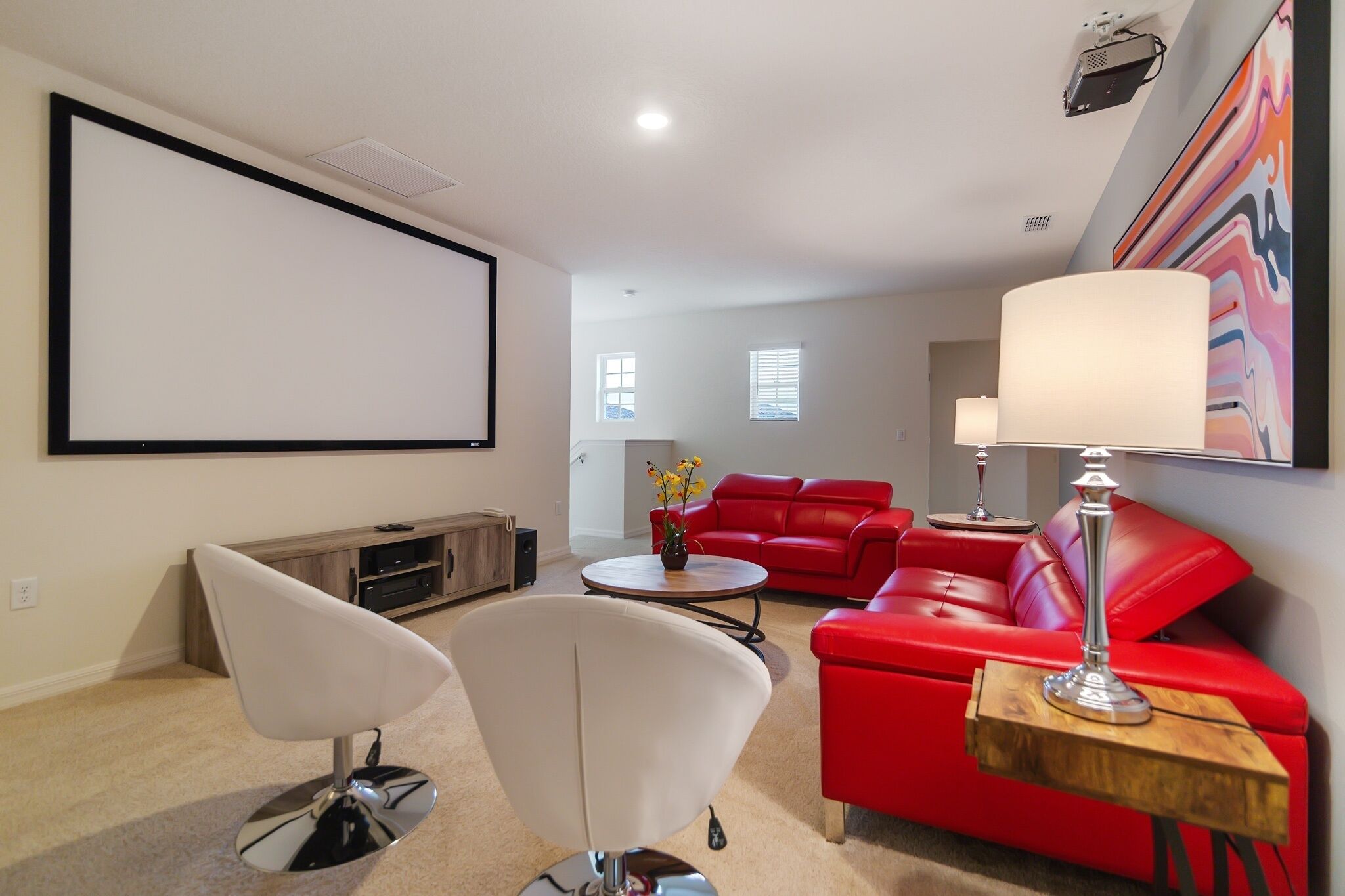 Un salon avec un canapé rouge, un fauteuil blanc et un écran de projection fixé au mur.