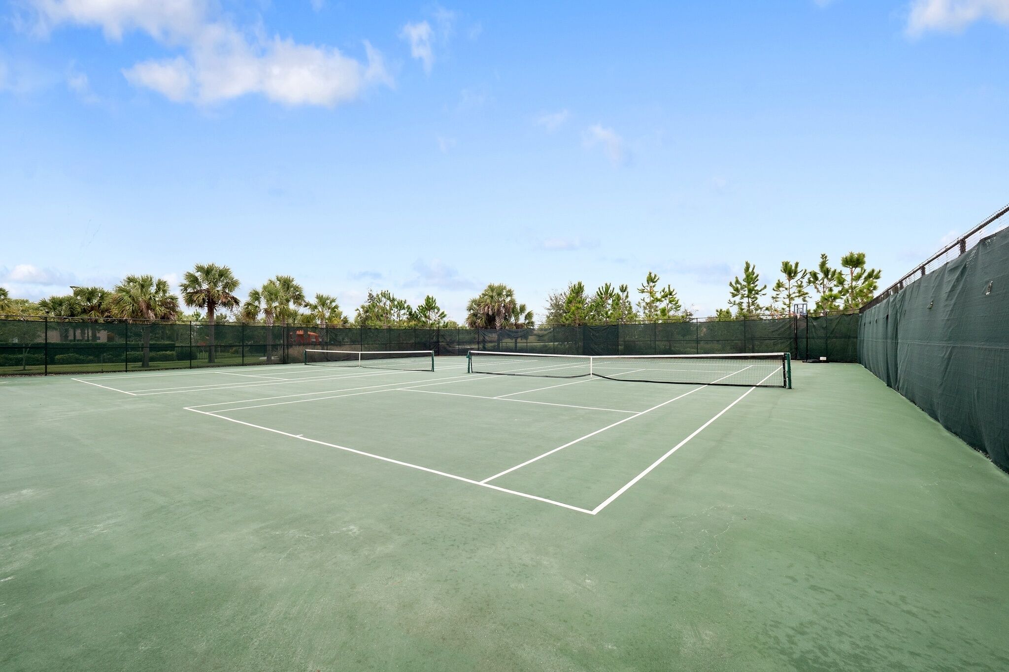 A tennis court with a net, surrounded by trees and a fence.