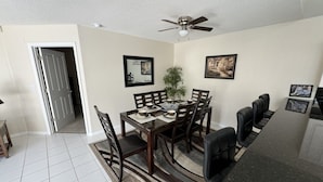 A dining area with a table set for four, a ceiling fan, and framed pictures on the walls. - Villa Crayson 3 Bedroom Home (Kissimmee)
