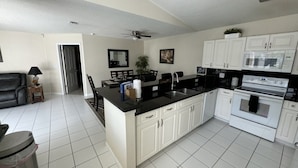A modern kitchen with white cabinets, a black countertop, and a built-in oven. - Villa Crayson 3 Bedroom Home (Kissimmee)