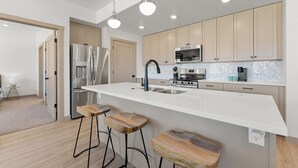 Une cuisine moderne dotée d’un grand îlot central, d’appareils électroménagers en acier inoxydable et de tabourets en bois.