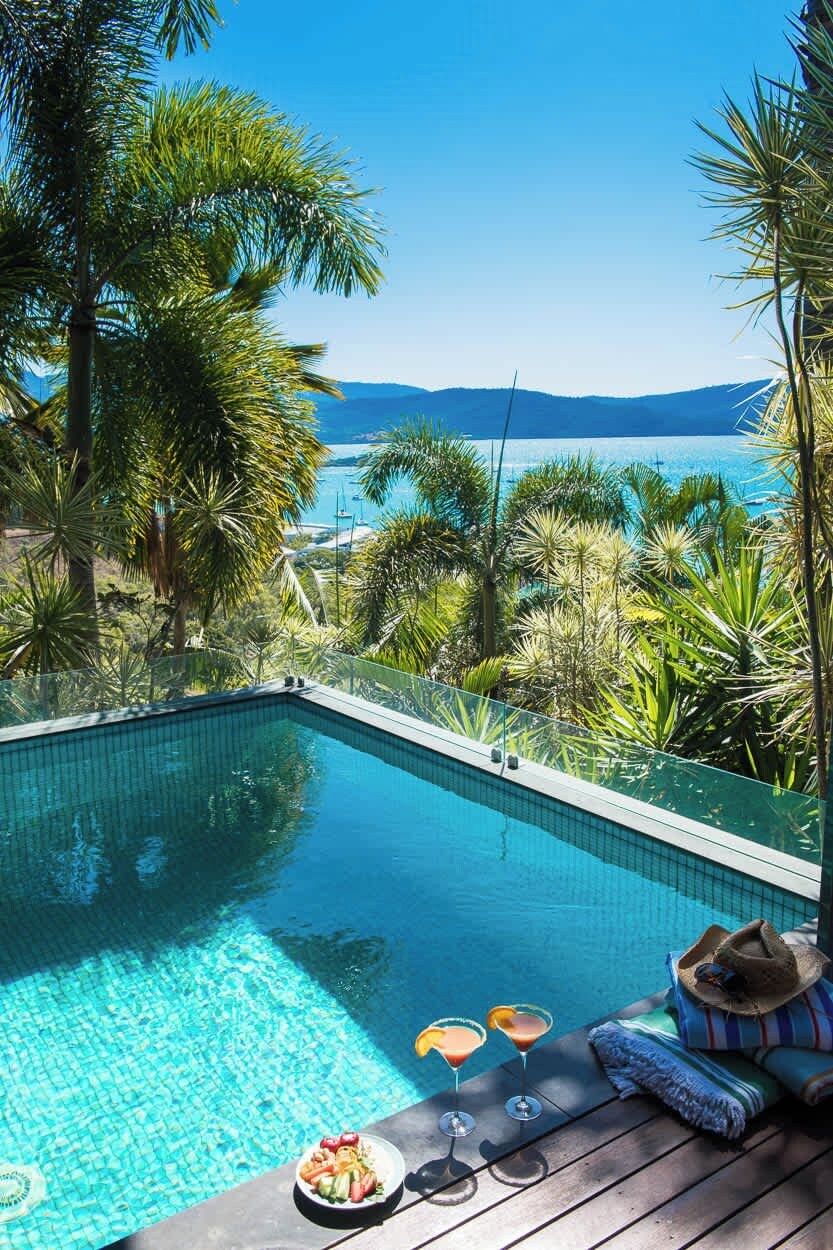 Une piscine à l’eau d’un bleu cristallin, entourée d’une végétation tropicale et offrant une vue sur une étendue d’eau.