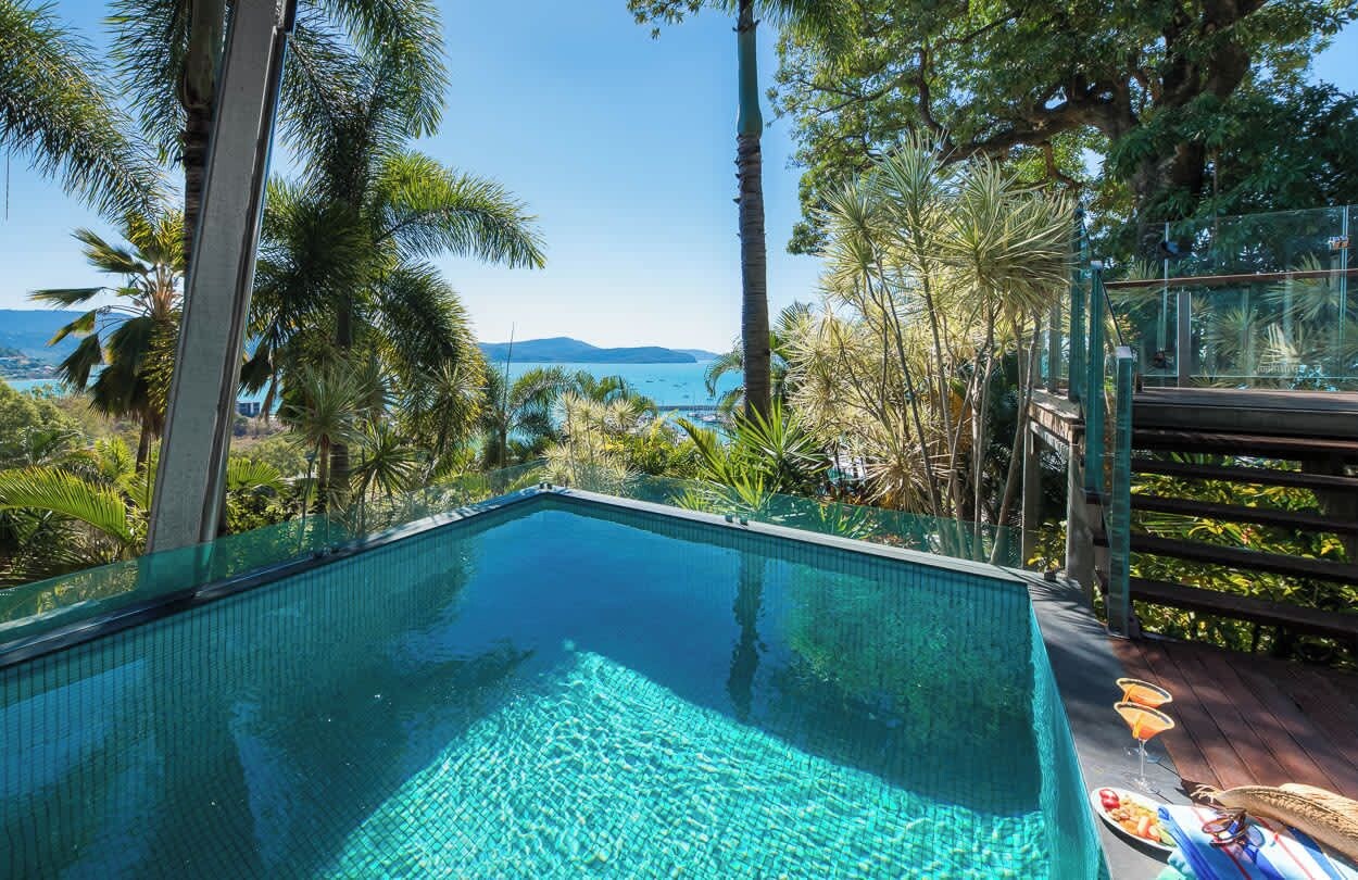An infinity pool with clear water, surrounded by tropical vegetation and overlooking a body of water.