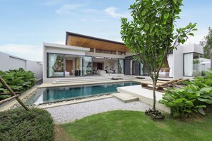 Una casa moderna con piscina, area relax esterna e vegetazione lussureggiante.