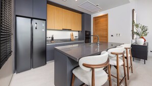 A modern kitchen with a central island, bar stools, and a wooden door. - Villa Eden by Tropiclook (Choeng Thale)