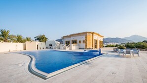 Une piscine avec une terrasse carrelée, un bâtiment à la façade jaune et des palmiers en arrière-plan.