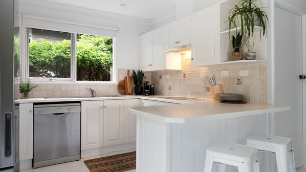 A modern kitchen with white cabinetry, a Bosch dishwasher, a large window with greenery outside, and a countertop with kitchen utensils.