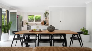 Una cocina moderna con armarios blancos, un ventanal grande y una zona de comedor con mesa de madera y sillas negras.