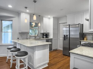 A modern kitchen with white cabinetry, a central island with bar stools, stainless steel appliances, and pendant lighting. - Near Beach Rental with Private Heated Pool & Putting Green | Isle of Palms (Isle of Palms)