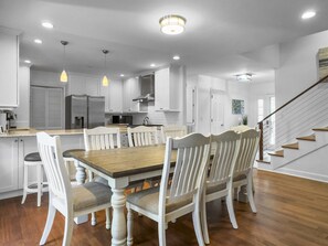 A modern kitchen with white cabinetry, a wooden dining table, and a staircase leading to another level. - Near Beach Rental with Private Heated Pool & Putting Green | Isle of Palms (Isle of Palms)