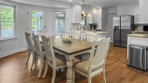 Une cuisine moderne avec des meubles blancs, des appareils en acier inoxydable et une table à manger en bois, accompagnée de six chaises.