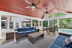 A sunroom with a wooden ceiling, a blue sofa, a dining table with chairs, and a view of the outdoors. - Near Beach Rental with Private Heated Pool & Putting Green | Isle of Palms (Isle of Palms)
