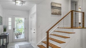 Un intérieur moderne avec un escalier en bois, des murs blancs et une porte donnant sur l’extérieur.