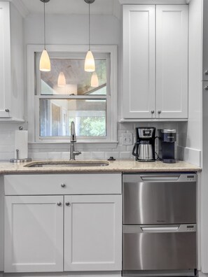 A modern kitchen with white cabinetry, a stainless steel dishwasher, a coffee maker, and pendant lighting. - Near Beach Rental with Private Heated Pool & Putting Green | Isle of Palms (Isle of Palms)