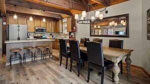 A rustic kitchen with wooden beams, a central island with stools, and a dining table with chairs. - Chambers Dreamin'-Chambers Beach, Pool & Tennis, Beautiful 3 bedroom, 2 bath (Homewood)
