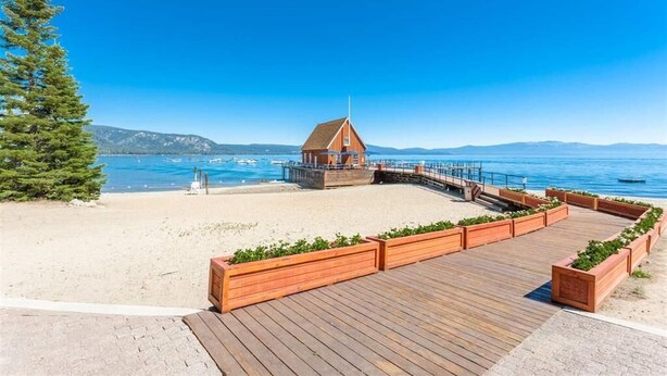 A wooden boardwalk leading to a small wooden building with a flagpole, overlooking a beach with clear blue water and distant mountains. - Chambers Dreamin'-Chambers Beach, Pool & Tennis, Beautiful 3 bedroom, 2 bath (Homewood)