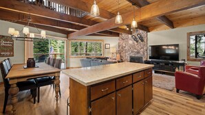 A spacious living area with a large wooden dining table, a stone fireplace, and a television. - Chambers Dreamin'-Chambers Beach, Pool & Tennis, Beautiful 3 bedroom, 2 bath (Homewood)