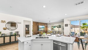 A modern kitchen with a central island, white cabinetry, and a dishwasher. - New Pool+Spa+Games+Large BBQ+Designer+Beautiful (Coachella)
