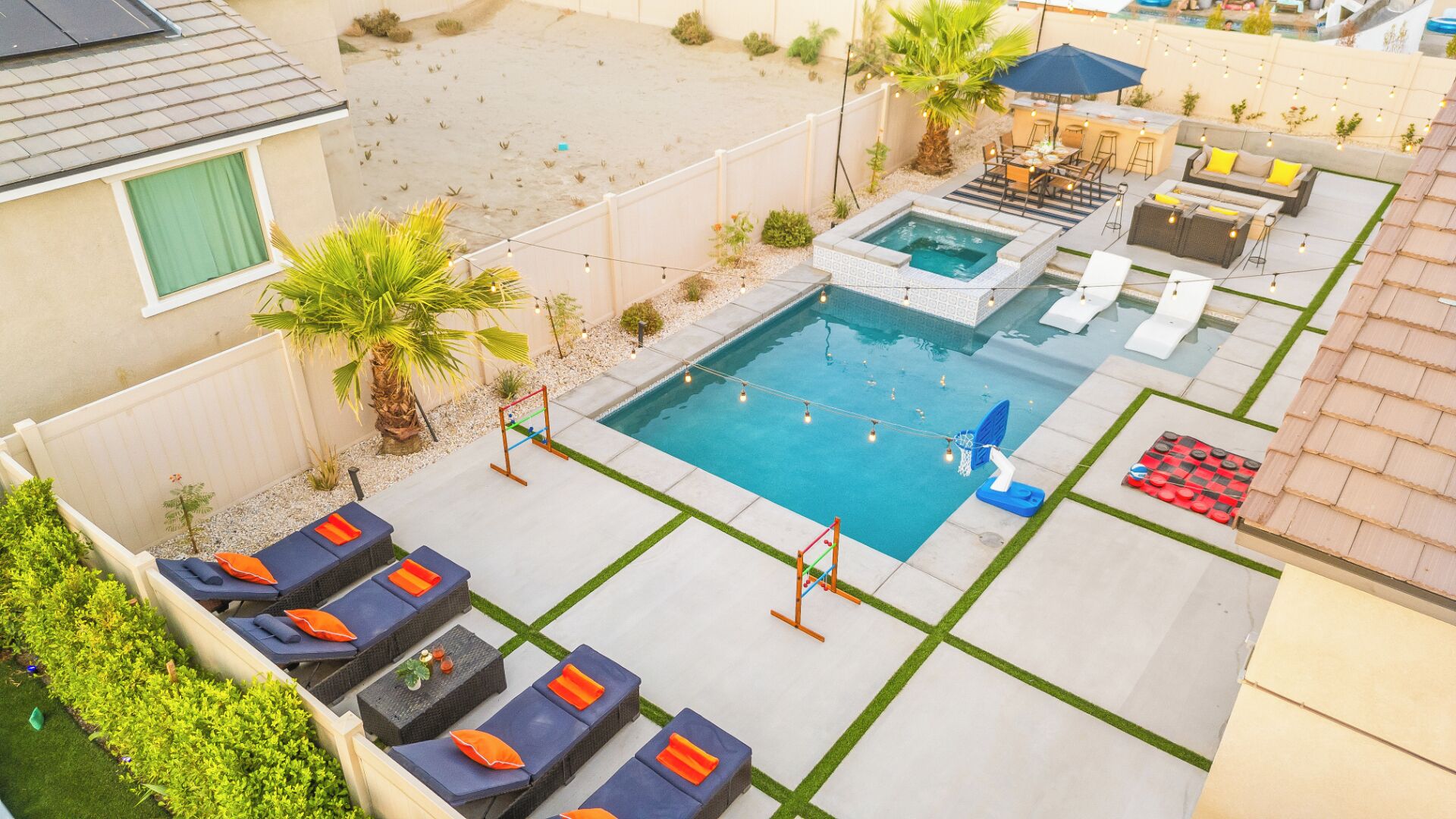 A backyard with a swimming pool, lounge chairs, a hot tub, and a barbecue area.