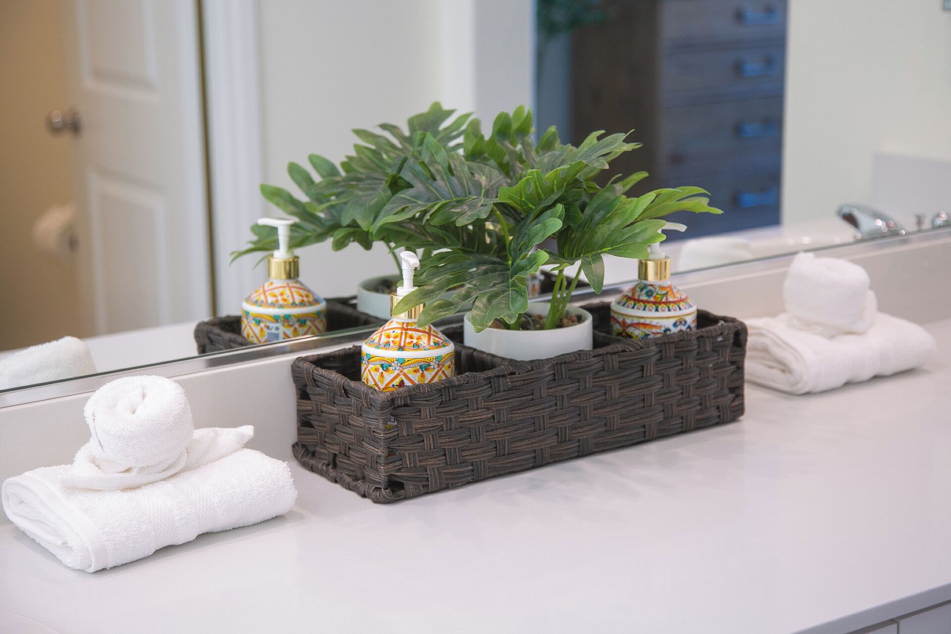 Een badkamer met een spiegel, een wastafel en een decoratieve plant in een gevlochten mand.