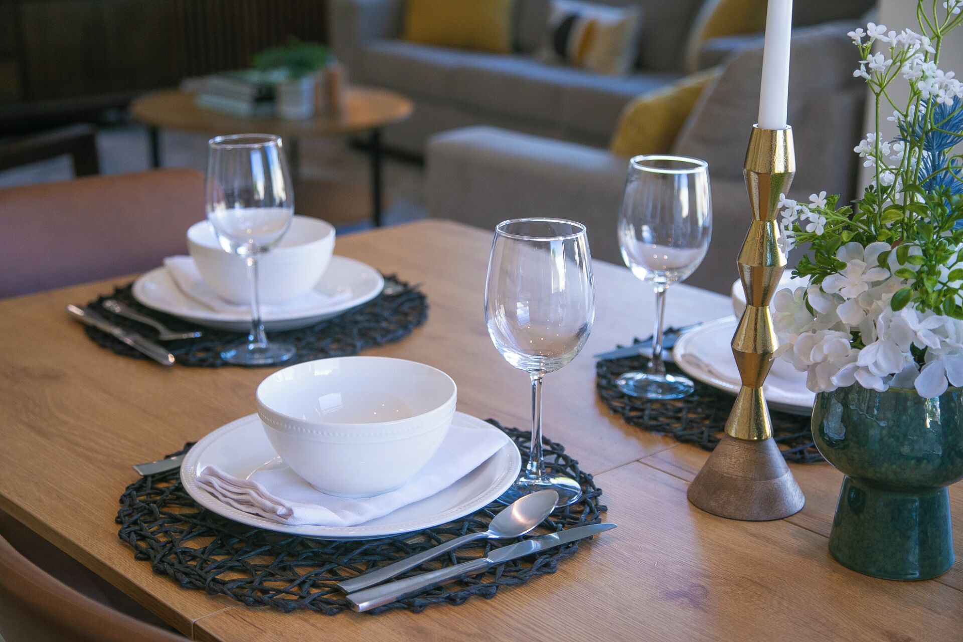 A dining table set with white plates, bowls, and cutlery, accompanied by wine glasses and a candle holder.