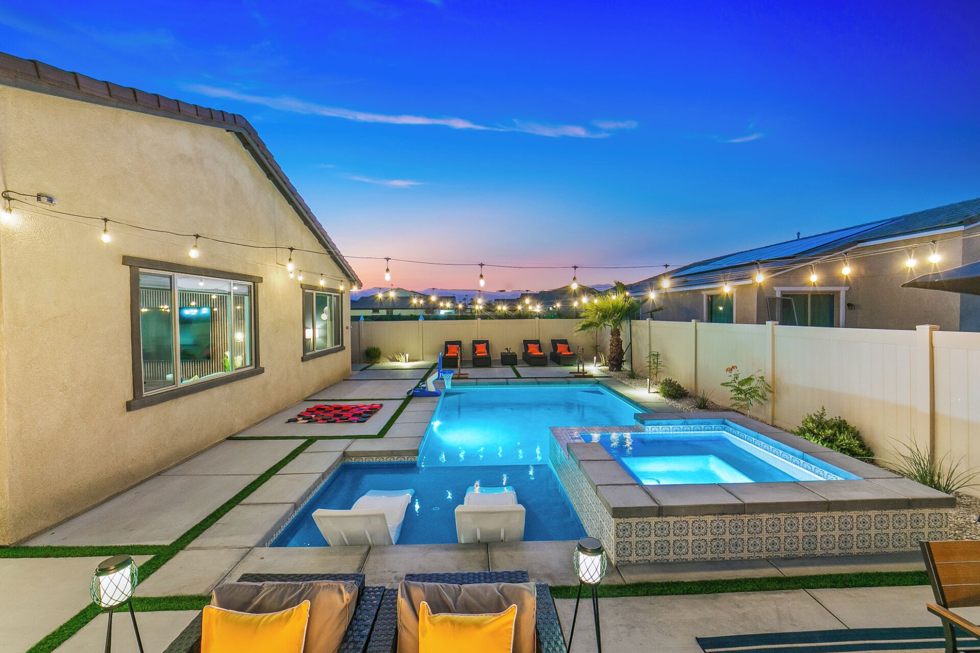 Un patio trasero con piscina, mobiliario exterior e iluminación con luces colgantes.