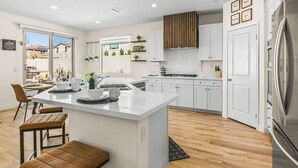 A modern kitchen with white cabinetry, a central island, and a stainless steel refrigerator. - New Pool+Spa+Games+Large BBQ+Designer+Beautiful (Coachella)