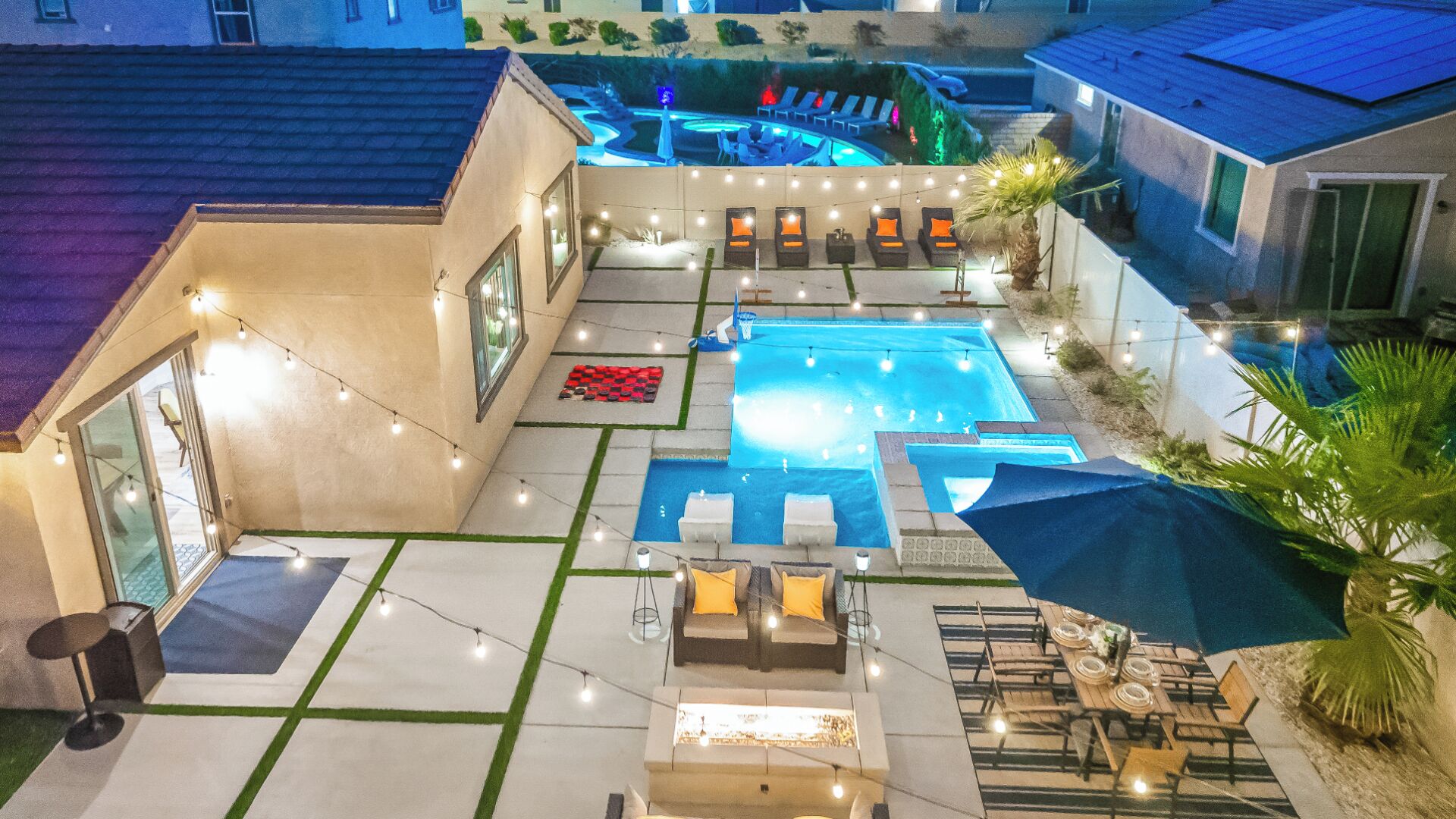 Un patio trasero con piscina, mobiliario exterior e iluminación colgante.