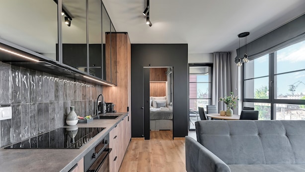 A modern kitchen with a grey countertop, wooden cabinets, and a grey sofa in the living area. - Doki Living & Foodhall by Downtown Apartments (Gdansk)