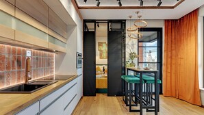 A modern kitchen with a black sink, wooden countertop, and a glass backsplash. There is a dining area with a table and chairs, and a view of a construction site through a window. - Doki Living & Foodhall by Downtown Apartments (Gdansk)