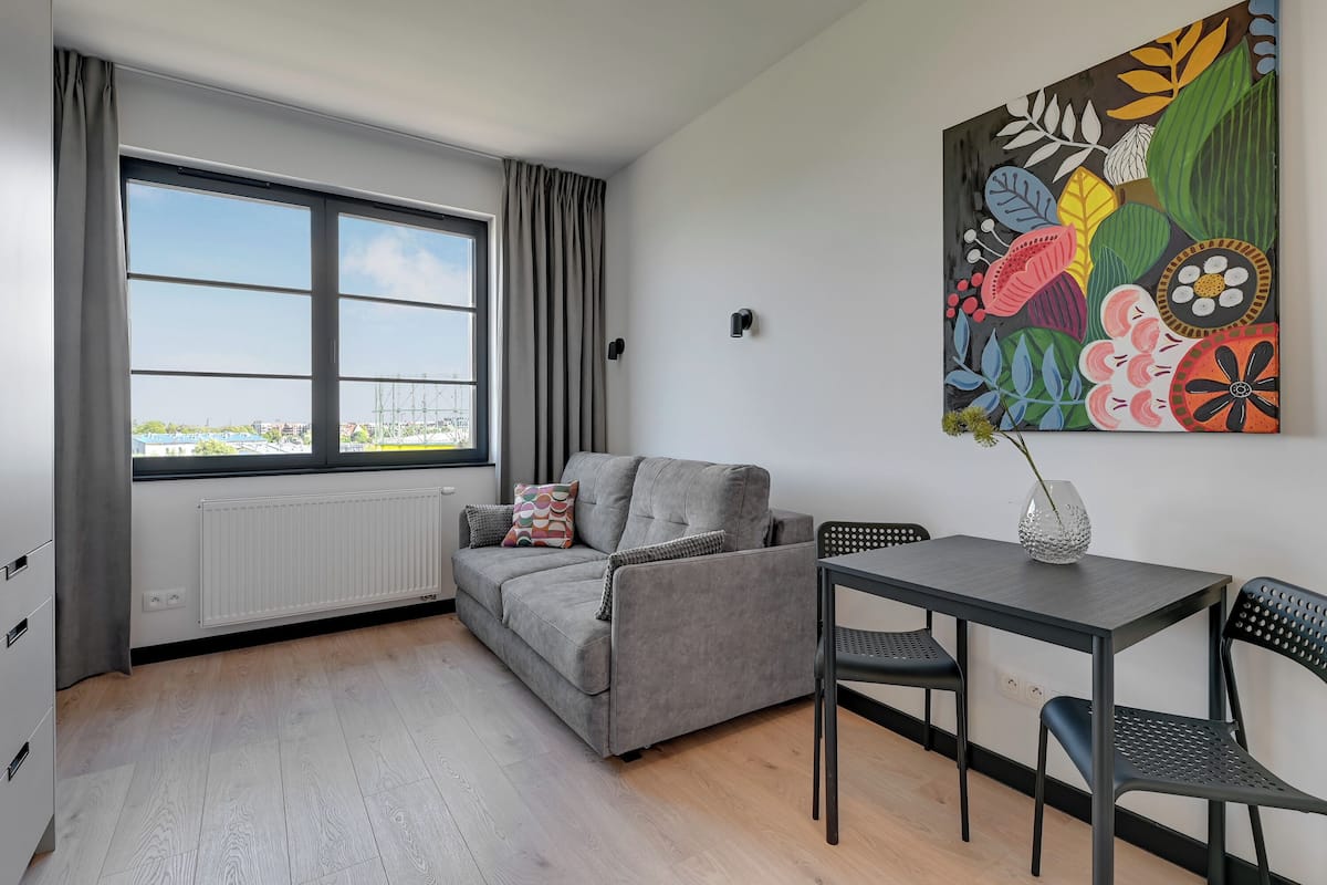 A modern living room with a grey sofa, a small table, and a colorful abstract painting on the wall.
