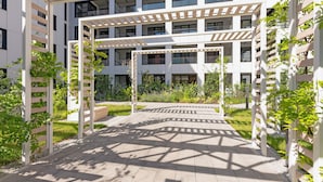 A modern building with multiple floors, a covered outdoor area with a pergola, and greenery around. - Doki Living & Foodhall by Downtown Apartments (Gdansk)