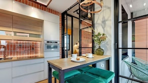 A modern kitchen with a brick backsplash, a wooden countertop, and a green upholstered bench. - Doki Living & Foodhall by Downtown Apartments (Gdansk)
