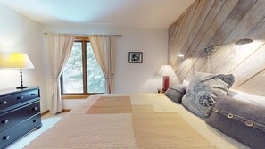 Een slaapkamer met een bed, nachtlampjes, een dressoir, een raam met gordijnen, en een houten hoofdeinde.