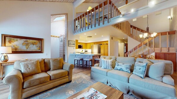 Un espacio habitable amplio con un techo alto, una cocina con armarios de madera y una escalera que conduce a un nivel superior.