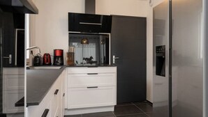 A modern kitchen with white cabinetry, a stainless steel refrigerator, and a black countertop.