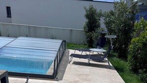 A rooftop pool area with a chair, a table, and a small table with chairs.